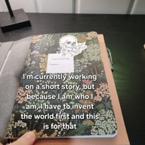 Dark green notebook with floral accents and a sticker of a skull. The notebook is labeled "ZOMBIES." text: "I am currently working on a short story, but because I am who I am, I have to invent the world first, and this is for that."