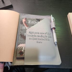 Back folder of notebook holding paperback. Text "Right now , one of the books I'm reading is thin so I just tucked it in there."